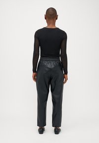 Haut en maille noir à manches longues associé à un pantalon taille haute en simili cuir noir brillant, doté d'une taille partiellement élastique et de poches latérales.
