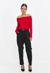 Rotes schulterfreies Rippenoberteil, kombiniert mit schwarzen High-Waist-Hosen, die ein elegantes Design und silberne Hardware-Details aufweisen.