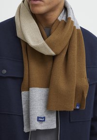 Knitted scarf in tan, beige, and light gray colors, featuring ribbed texture and contrasting patterns, with a blue label detail.