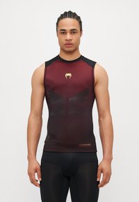Bordo krāsas bez piedurknēm sporta krekls ar melniem akcentiem, divertizēts ar teksturētu dizainu un zelta logotipu. Izgatavots no viegla, elpojoša materiāla.