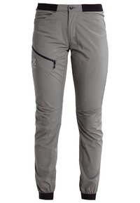 Lehké šedé venkovní kalhoty s úzkým střihem, elastickým pasem, zipovou boční kapsou a černými manžetami u kotníků. Hladká, odolná tkanina.