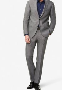 Gray checked suit with a tailored fit, single-breasted jacket, and flat-front trousers, paired with a navy blue button-up shirt and black shoes.