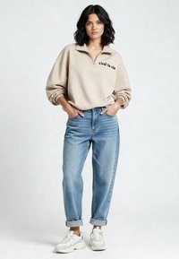 Felpa beige con zip e scritta "c'est la vie", abbinata a jeans a vita alta color azzurro chiaro e sneakers bianche. Vestibilità comoda con maniche risvoltate.