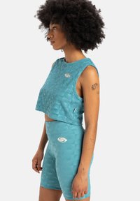 Teal atletski crop top i odgovarajuće visoke kratke hlače s teksturiranim uzorcima; sadrži logo i detalje šivanja.