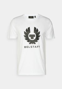 Camiseta de algodón blanca con un gran logo gráfico negro con alas y el texto "BELSTAFF" en la parte inferior. Cuello redondo, mangas cortas.