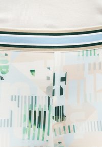 Κοντινή λήψη υφάσματος με γεωμετρικά παστέλ σχήματα και κάθετες ρίγες σε πράσινο, μπλε, μπεζ και λευκό, με ριγέ ζώνη στη μέση.