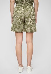 Shorts fleuris verts avec une taille élastique, fabriqués en tissu léger. Le design présente un motif botanique de couleur claire.