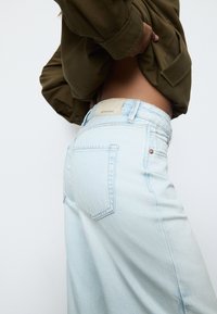 Jasnoniebieskie dżinsy z denimu z wysokim stanem, z postrzępionym brzegiem, dwoma tylnymi kieszeniami oraz beżową skórzaną metką na pasie. Gładka faktura.