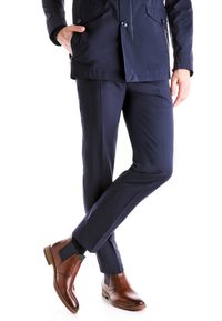 Veste navy avec poches, pantalon navy ajusté et bottines en cuir marron avec côtés élastiques. Lignes épurées et design élégant.
