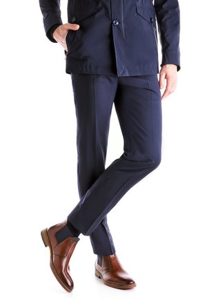 Veste navy avec poches, pantalon navy ajusté et bottines en cuir marron avec côtés élastiques. Lignes épurées et design élégant.
