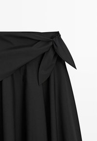 Zwarte jurk met een brede, gedrapeerde kraag en een gestrikte knoop. Glad materiaal met een vloeiende silhouet en subtiele textuur. Ritssluiting aan de achterkant.