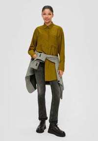 Olijfgroene lange mouwen shirt met twee borstzakken, gecombineerd met donkergrijze jeans en zwarte plateau laarzen. Een geruit jack om de taille geknoopt.