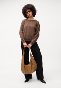 Brun sweatshirt med en afslappet pasform, sorte vide bukser og en tan skuldertaske lavet af tekstureret materiale. Tilbehøret inkluderer briller med skildpaddemønster.