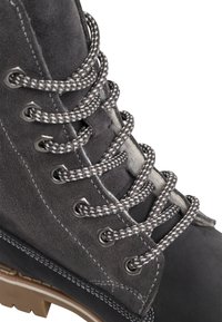 Grauer Wildlederstiefel mit dicken grau-weißen Schnürsenkeln, silbernen Ösen und kontrastierenden Nähten. Verfügt über eine robuste Sohle und eine strukturierte Oberfläche.