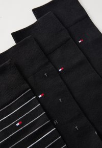 Sorte sokker med varierende designs: en ensfarvet, en med vandrette hvide striber, hver med et lille logo med rød, hvid og blå accent.