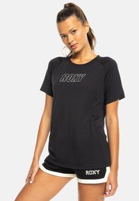 Czarny T-shirt z logo "ROXY" w białej czcionce, krótki rękaw, okrągły dekolt, wykonany z gładkiego materiału, zestawiony z czarnymi szortami z białymi akcentami.