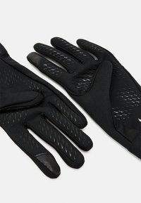 Gants noirs en tissu léger avec un motif de grip texturé, présentant un design ajusté et une finition lisse sur les bouts.
