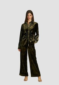 Camisa de botón de terciopelo verde oliva con fruncido en la parte delantera, combinada con pantalones de pierna ancha a juego. Ambas prendas cuentan con una textura suave y lisa.