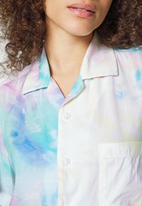 Camicetta con bottoni realizzata in tessuto leggero, caratterizzata da un motivo tie-dye pastello con colori tenui come blu, rosa e bianco. Include una tasca.