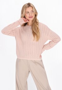 Trui in zachtroze, met een gestructureerd gebreid patroon, ronde halslijn en een losse pasvorm, gecombineerd met lichtbeige broek.