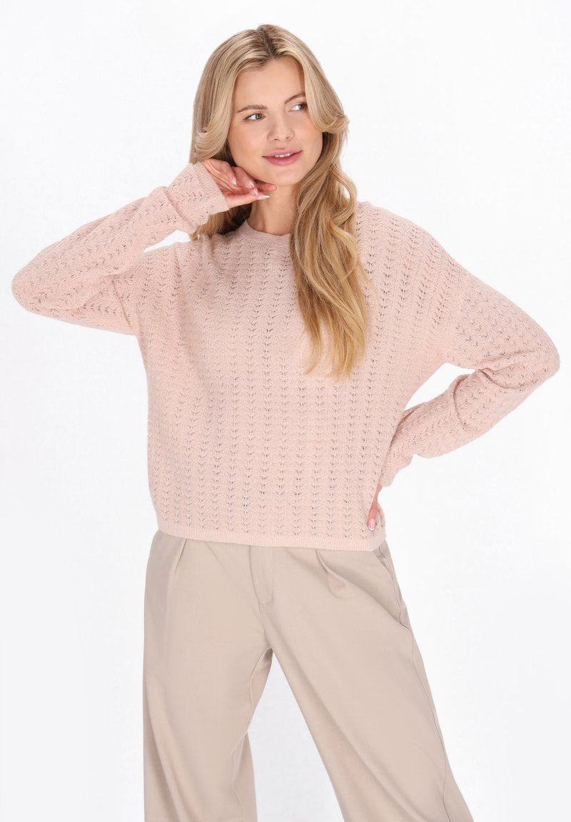 Trui in zachtroze, met een gestructureerd gebreid patroon, ronde halslijn en een losse pasvorm, gecombineerd met lichtbeige broek.