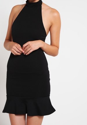 Femme portant une robe noire sans manches à col halter, taille cintrée et ourlet évasé sur fond blanc uni.