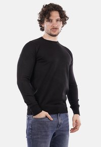 Maglione nero a maniche lunghe con collo a giro, texture lavorata a maglia e polsini e orlo a costine, abbinato a jeans blu.