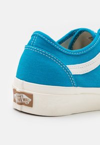 Baskets en toile bleue avec accents blancs, semelle en caoutchouc et coutures contrastantes. Patch logo visible au talon.