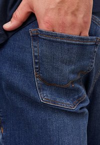 Χέρι μερικώς εισ inserted σε πίσω τσέπη σκούρων μπλε τζιν με ορατές πορτοκαλί ραφές.