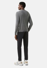 Grauer Strickpullover mit Rundhalsausschnitt, kombiniert mit schwarzen Hosen und weißen Sneakers. Mit gerippten Bündchen und Saum, glatte Textur.