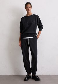 Zwarte sweatshirt met reliëf merknaam, ronde hals en geribde manchetten, gecombineerd met zwarte tapered joggers en zwarte loafers.