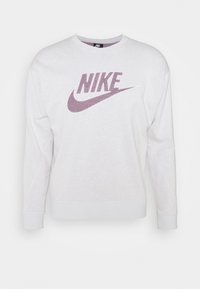 Sudadera blanca hecha de una tela suave, con un gran logo de Nike en color burdeos en la parte frontal. Cuello redondo estándar y mangas largas.