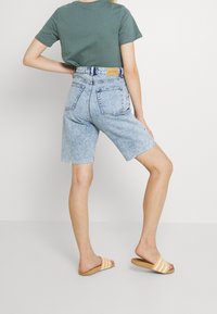 Ljusblå jeansshorts med fransig fåll, hög midja och bakfickor, kombinerade med en mörkgrön t-shirt och randiga slidesandaler.