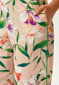 Floral-printed trousers in soft fabric, featuring pink background, green leaves, purple and orange flowers, and a side pocket.