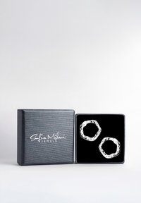 Silverörhängen i hoop-stil med en texturerad, vågig design, visade i en svart smyckeslåda fodrad med sammet och med en metallisk grå utsida.