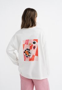 Witte blouse met lange mouwen met een kleurrijke grafische print op de achterkant, met abstracte vormen en een patroonontwerp.