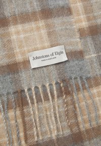 Plaid scarf in shades of gray, brown, and beige, made from soft wool, featuring fringed ends and a label stating "Johnstons of Elgin, Made in Scotland."