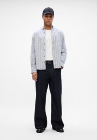 Gaišas pelēks krekls ar vertikālām svītrām, uzvilkts virs balta tank topa. Apvienots ar platām tumšām džinsu biksēm un melnām kurpēm.