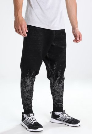 Schwarze Jogginghose aus strukturiertem Stoff mit einem Farbverlauf, der unten zu Grau ausläuft. Kombiniert mit schwarzen Sportschuhen.