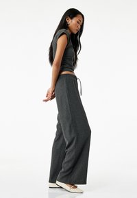 Grijze geribbelde crop top met korte mouwen, gecombineerd met wijde grijze broeken met een trekkoord in de taille. Glad textuur balletschoenen.