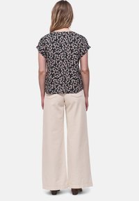 Top nero a maniche corte con motivo floreale rosa; abbinato a pantaloni beige a gamba larga; tessuto leggero e vestibilità comoda in toni neutri.
