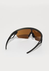 Braun getönte Sonnenbrille mit schwarzem Rahmen, die ein geschwungenes Design und verstellbare Nasenpads aufweist. Leicht und mit sportlicher Ästhetik.