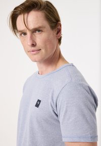 Camiseta texturizada de color azul claro con un parche de logo marino en el pecho. Mangas cortas y cuello redondo. Tejido suave con un ajuste holgado.