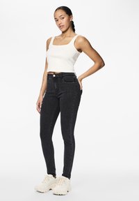 Črne visoke skinny kavbojke s klasičnim pet-im postopkom, kombinirane z belo rebrasto skrajšano majico in debelimi belimi športnimi copati.
