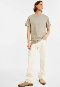 Lys beige bomulds t-shirt med korte ærmer, sat sammen med off-white lige bukser og lyse brune ankelstøvler. Enkel, udekoreret design.