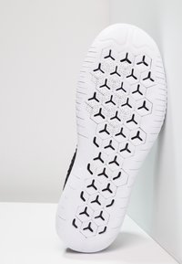 Schoenzool met een witte rubberen basis met een honingraatpatroon, geaccentueerd met zwarte vormen die op een logo lijken. Geprofileerd voor grip.