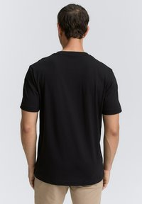 Sort kortærmet t-shirt lavet af et glat, blødt stof, med en klassisk rund hals og en afslappet pasform. Tekstureret ryg med minimal design.