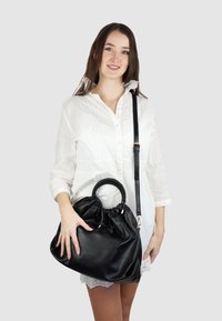 Zwarte leren tas met een gematteerde afwerking, voorzien van een gevlochten handvat, een trekkoordsluiting en een verstelbare schouderriem.