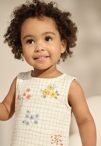 Varrukateta kleit kreemikas kangas, ruudulise mustriga. Kaunistatud mitmevärviliste lillelise tikandiga. Sile tekstuur, juhuslik disain.