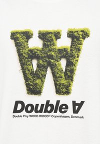 T-shirt branca com um grande 'W' coberto de musgo verde e texto preto a dizer "Double A" abaixo, com detalhes adicionais da marca por baixo.